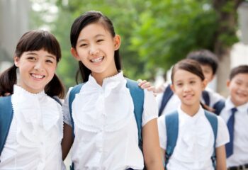 Happy Chinese schoolgirls in uniform with friends outdoors