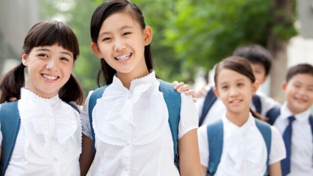 Happy Chinese schoolgirls in uniform with friends outdoors Happy Chinese schoolgirls in uniform with friends outdoors