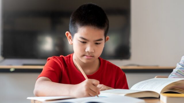 Image of a young Asian boy taking notes from studying in the classroom